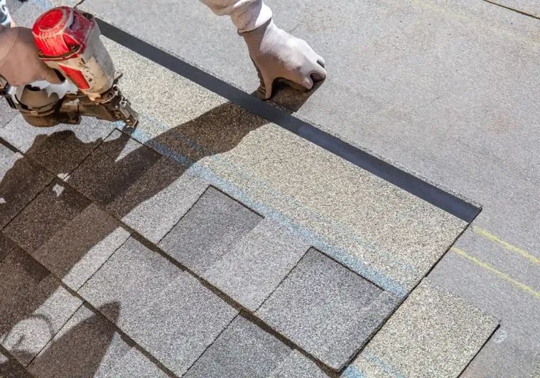Roofer replacing damaged shingles by hand